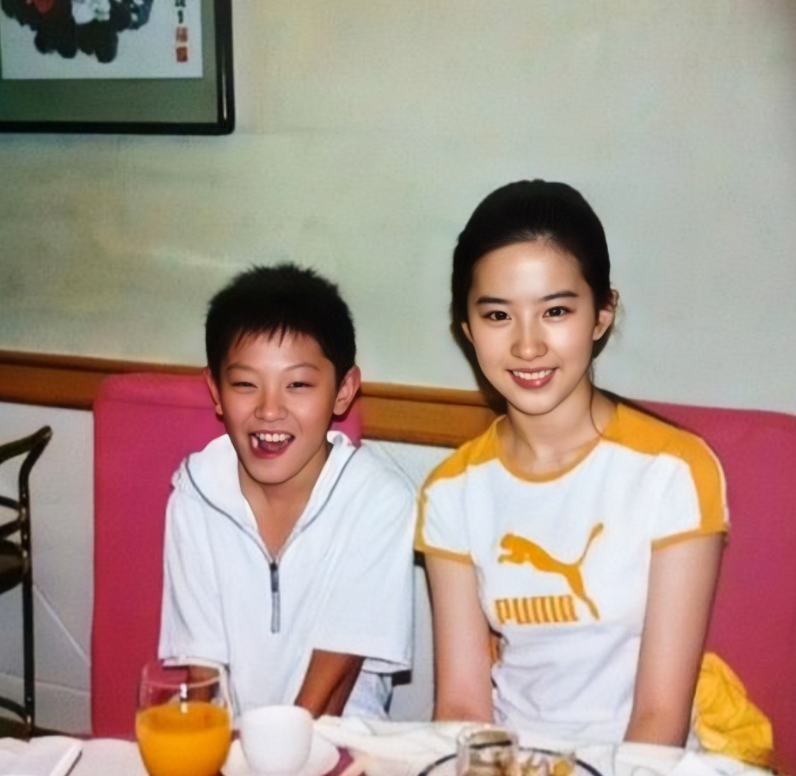 这是2002年夏天，小男孩与刘亦菲在饭桌上的合影。转眼二十多年过去了，当年那个坐
