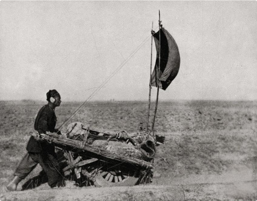 这张照片里藏着晚清底层劳动者的巧思，开阔的荒地上，男子弓身推着独轮车，车斗上却支