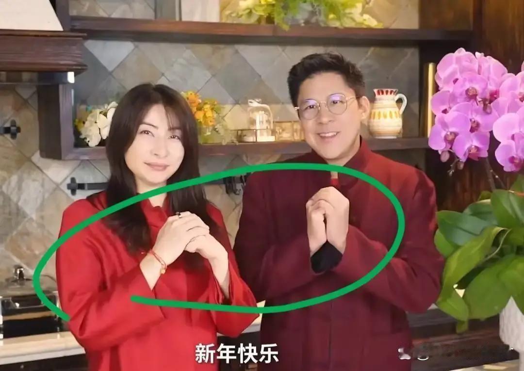 霍启刚左手包住右拳。郭晶晶右手包住左拳。视频里两人穿着红衣服，背后挂着灯笼，用