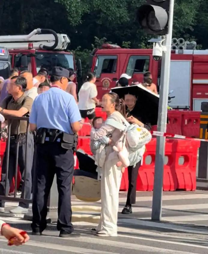 三十多度的大热天，一位妈妈抱着孩子、拎着儿童座椅和大包行李，被拦在马拉松赛道边上