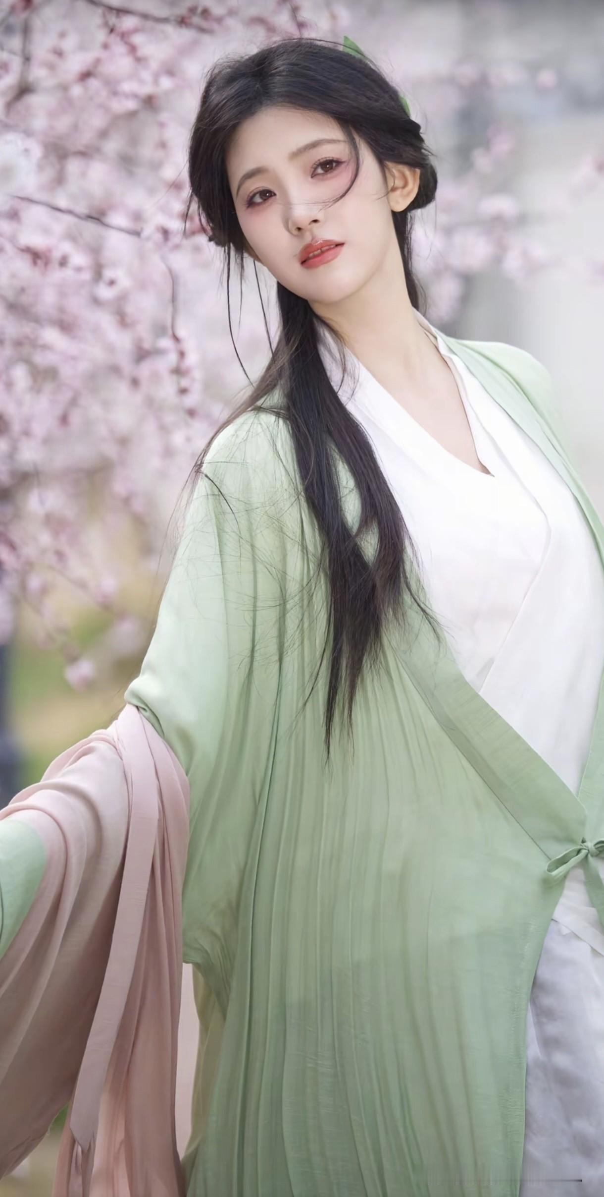春日樱花树下，身着绿衫的仙子轻挽衣袖，眼神温柔似水，仿佛从画中走出的江南少女，美