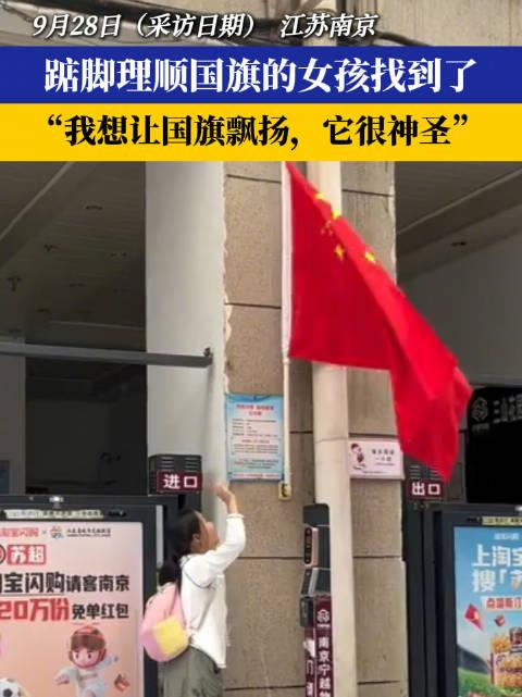 江苏南京，一位女孩路过一处门口，发现悬挂的五星红旗被门卡住了，她停下脚步，踮起脚