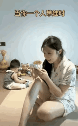 年轻的母亲和孩子在家，妈妈在一边玩着手机开心的笑，儿子坐在一边自己玩，当母亲回头