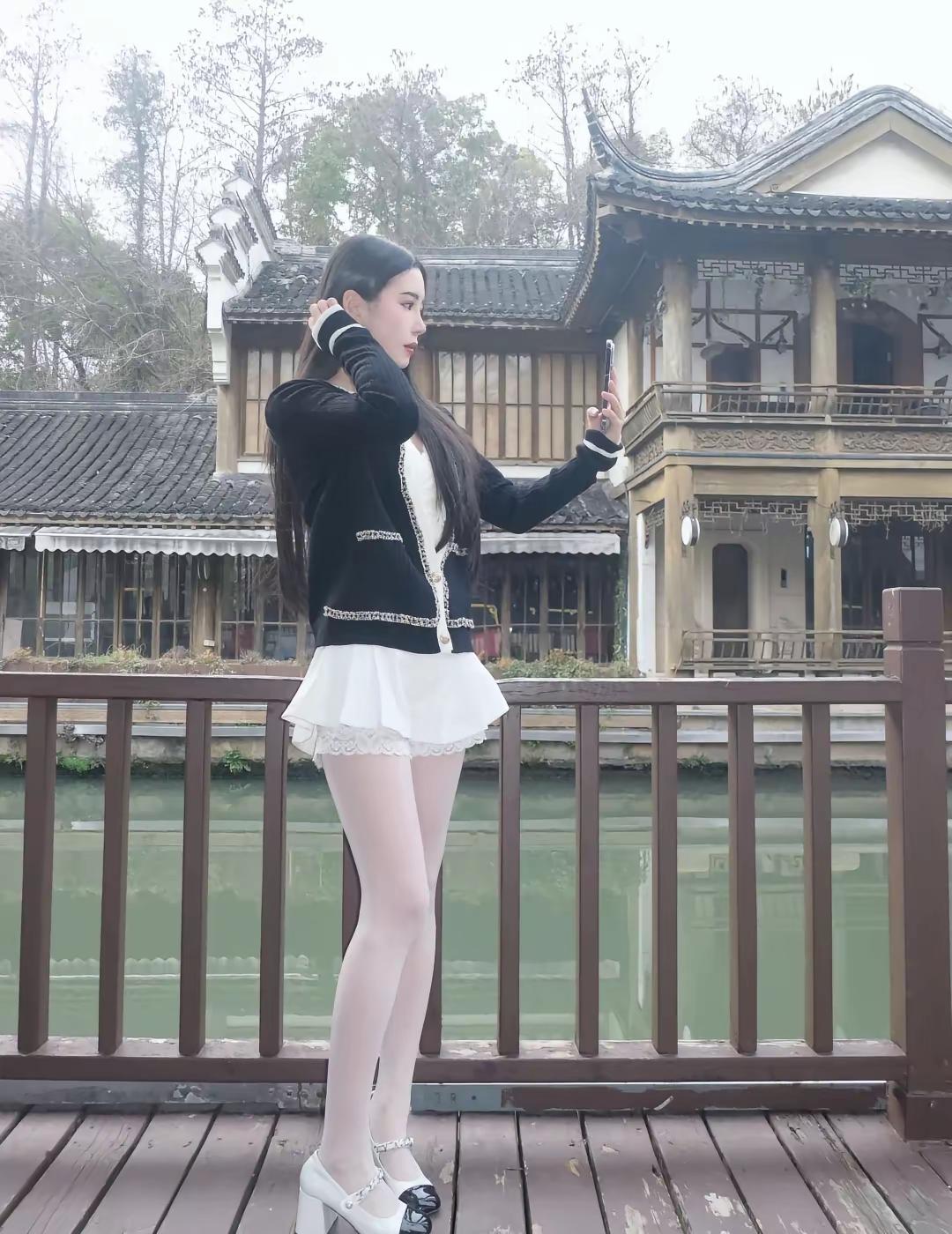 在古镇的桥上，少女自拍留念，古风建筑映衬，唯美如画。