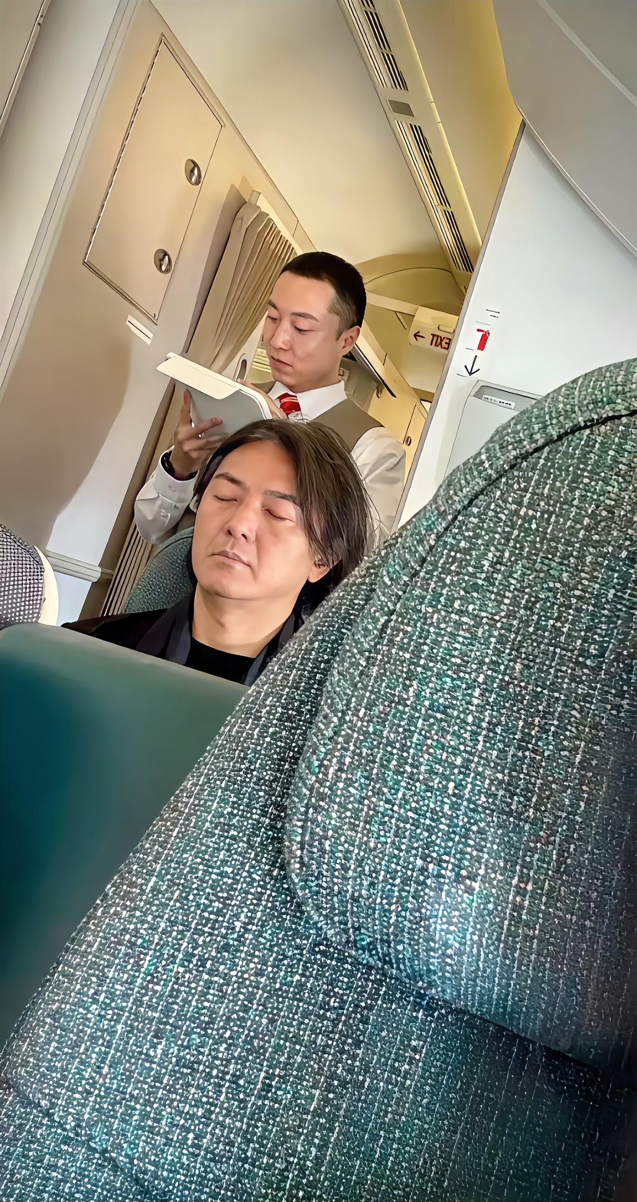这是郑伊健坐经济舱的画面，他坐在那里正在闭目休息中，头上已有白发丝了。郑伊健