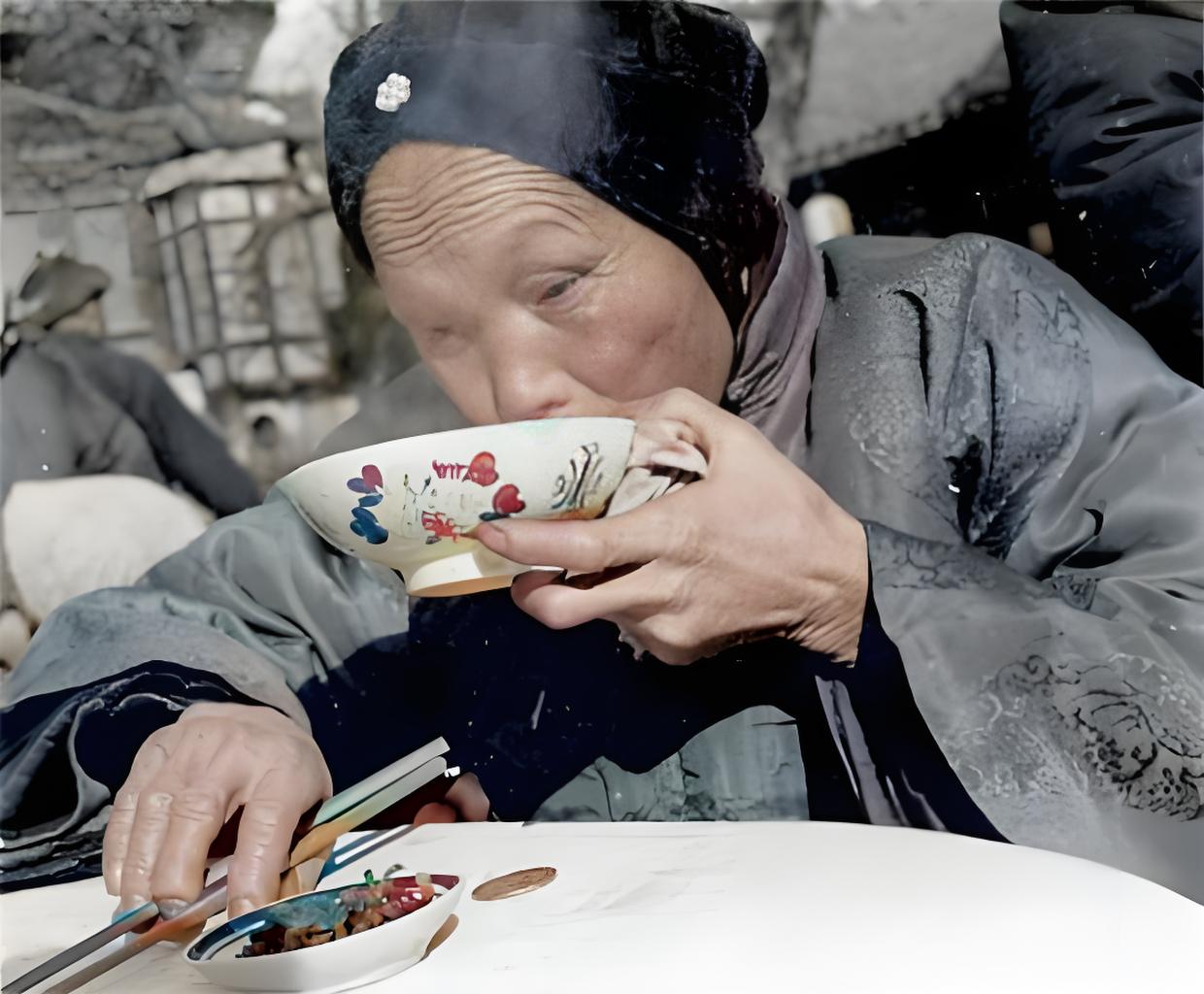 这是一张展现旧中国平民饮食场景的黑白照片。画面中一位老妇人正用手捧着带有花纹的瓷