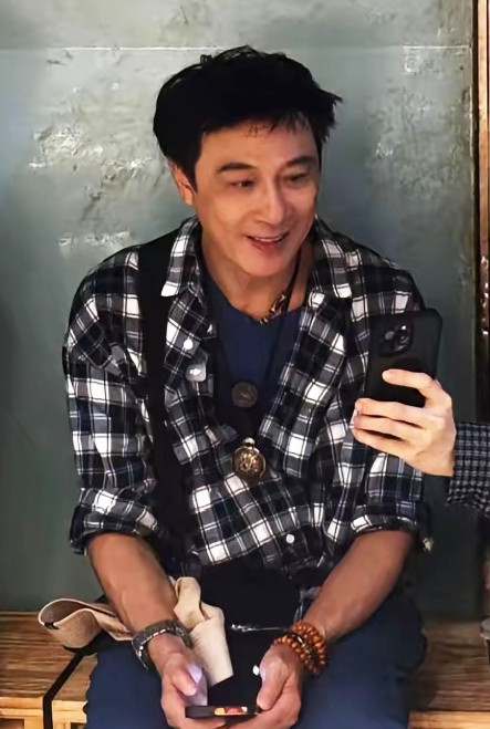 网友在成都旅游偶遇吴镇宇。一身黑白格衬衫配牛仔裤，米白渔夫帽，穿搭简单松弛。65岁身姿挺拔，笑容亲和