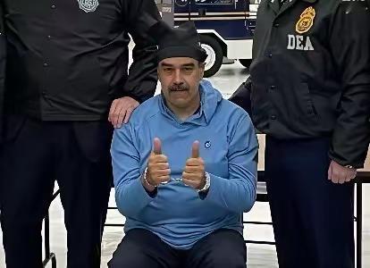 这是一张马杜罗被抓后的照片，他坐在一张椅子上，手上戴着手铐，伸出两个大拇指做出点