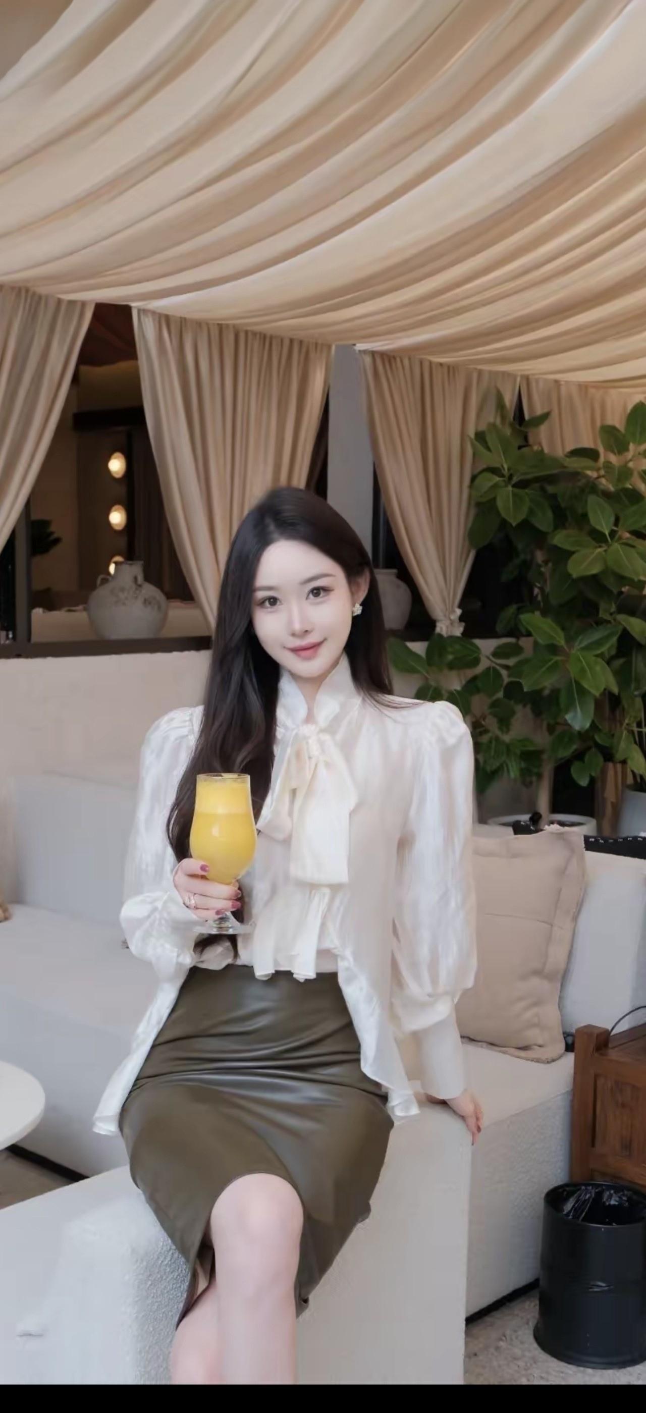 美女坐在沙发上，喝着橙汁，微笑。