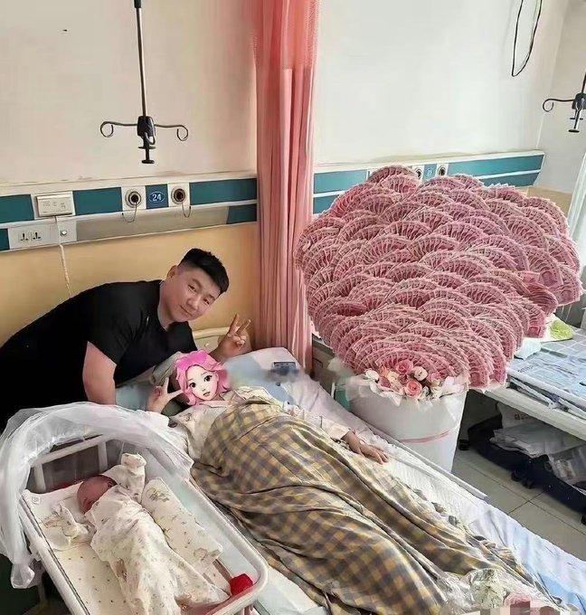 一女子产下一子，丈夫手捧一束用百元大钞折成的“有钱花”，鲜花配钞票，排面拉满。网
