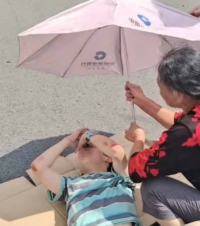 路人纸盒垫地撑伞遮阳守护伤者8月20日，江苏扬州一辆电动车与一辆轿车相撞