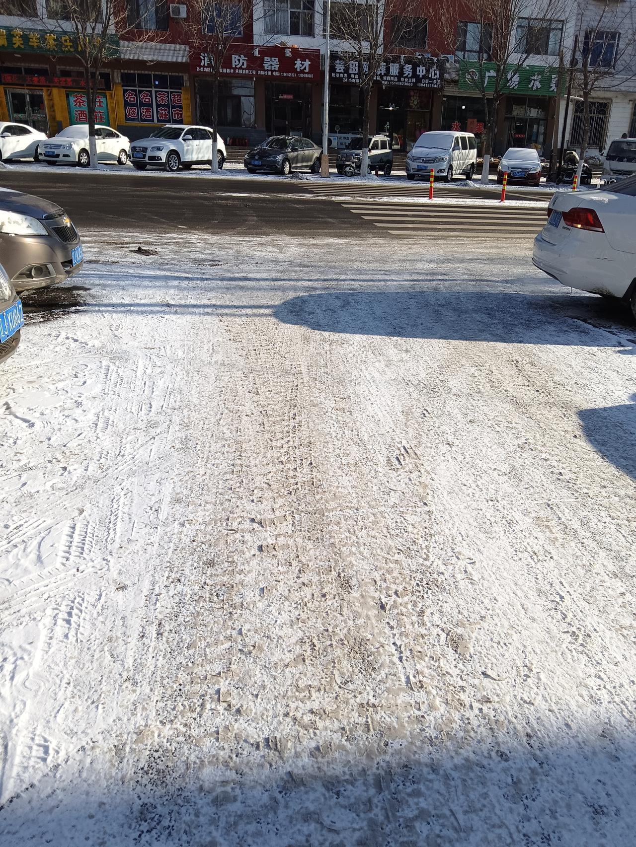 冬日雪景中的城市街景，车辆停靠在路边，阳光洒在积雪上，显得格外宁静。城市冬日雪景