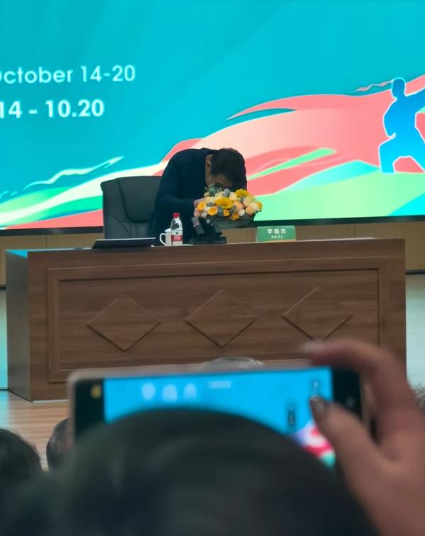 李连杰上台后准备发言，看到桌子上摆放的黄色花束，弯着腰小心翼翼拿到旁边。这个