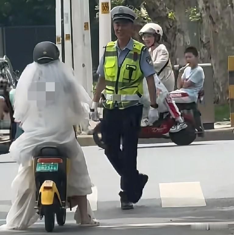 5月27日，湖北襄阳一交警正站在路口值勤，突然一女子穿着婚纱骑着两轮电动车过来，