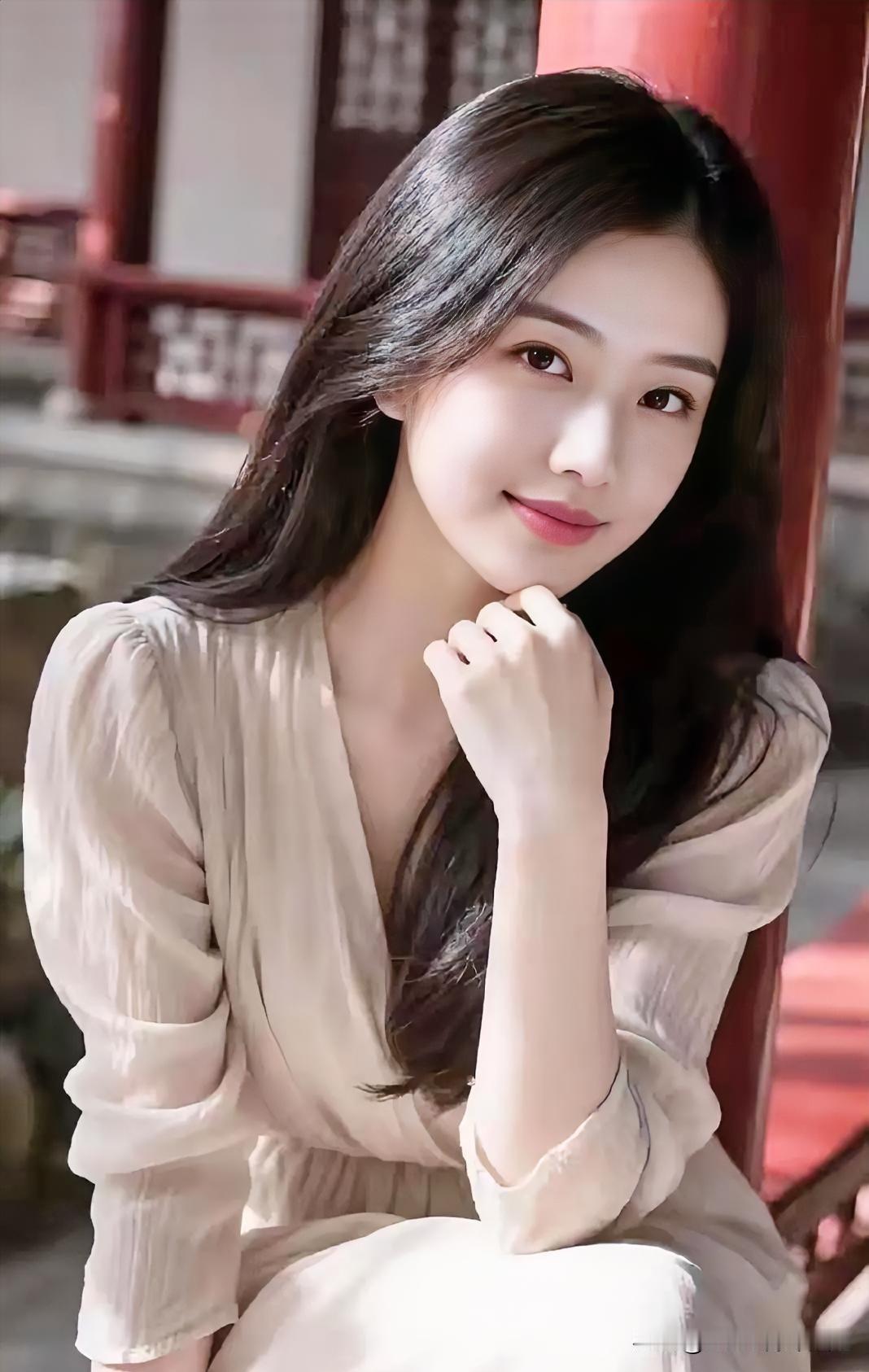 米色纱裙轻裹温婉身姿，长发披肩，倚柱浅笑。古建光影下，静谧柔和，尽显东方女子的含