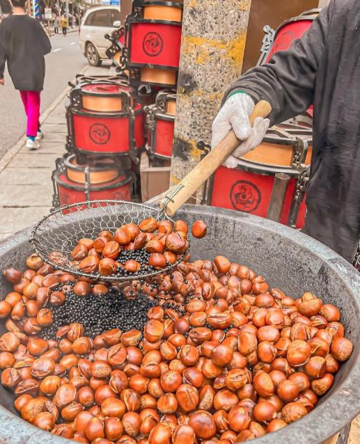 北京东城，一名大妈逛街时看到干果店内刚出炉的板栗，未经店家许可，直接上前拿起一颗