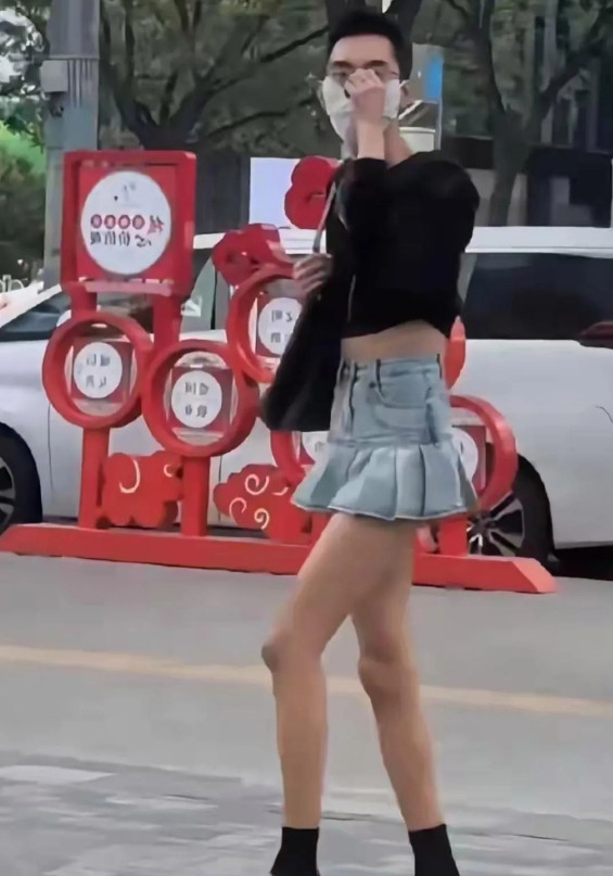 天呐，一个大男生竟身着超短牛仔裙、黑色露脐装还挎着女式坤包招摇过市，这般打扮难