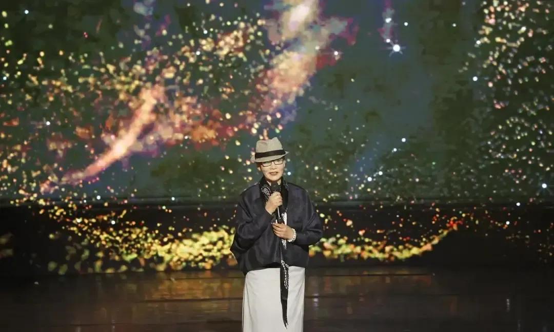 潘虹穿黑大衣配白高领站在上海论坛，七十岁背脊笔直，头发盘得一丝不苟。镜头扫过，