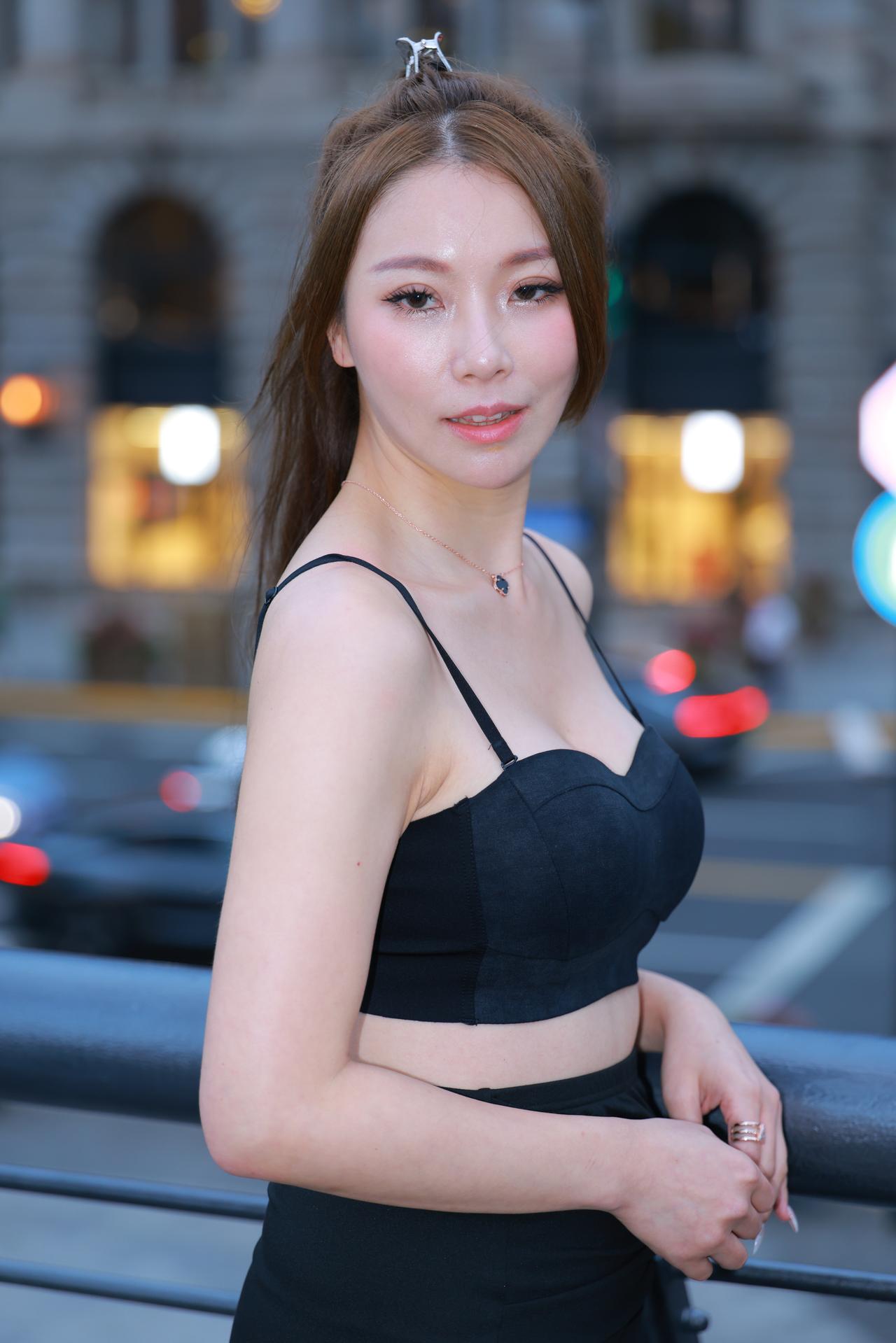 《晚风与笑眼》夜色漫过都市街头，暖红灯晕在她身后晕开朦胧光斑。她身着简约黑色