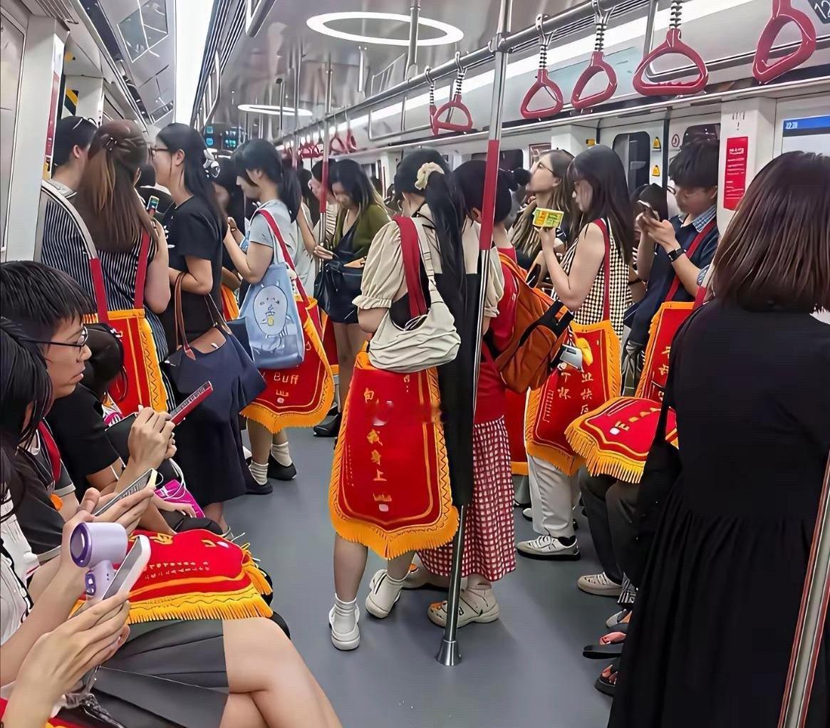地铁里偶遇新奇一幕，好多姑娘身上都披着同款红黄色锦旗，整车厢放眼望去格外醒目，场