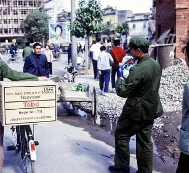 这是1981年广州一位男子买了一台电视机往家赶。男子将电视机放在自行车的后座上。