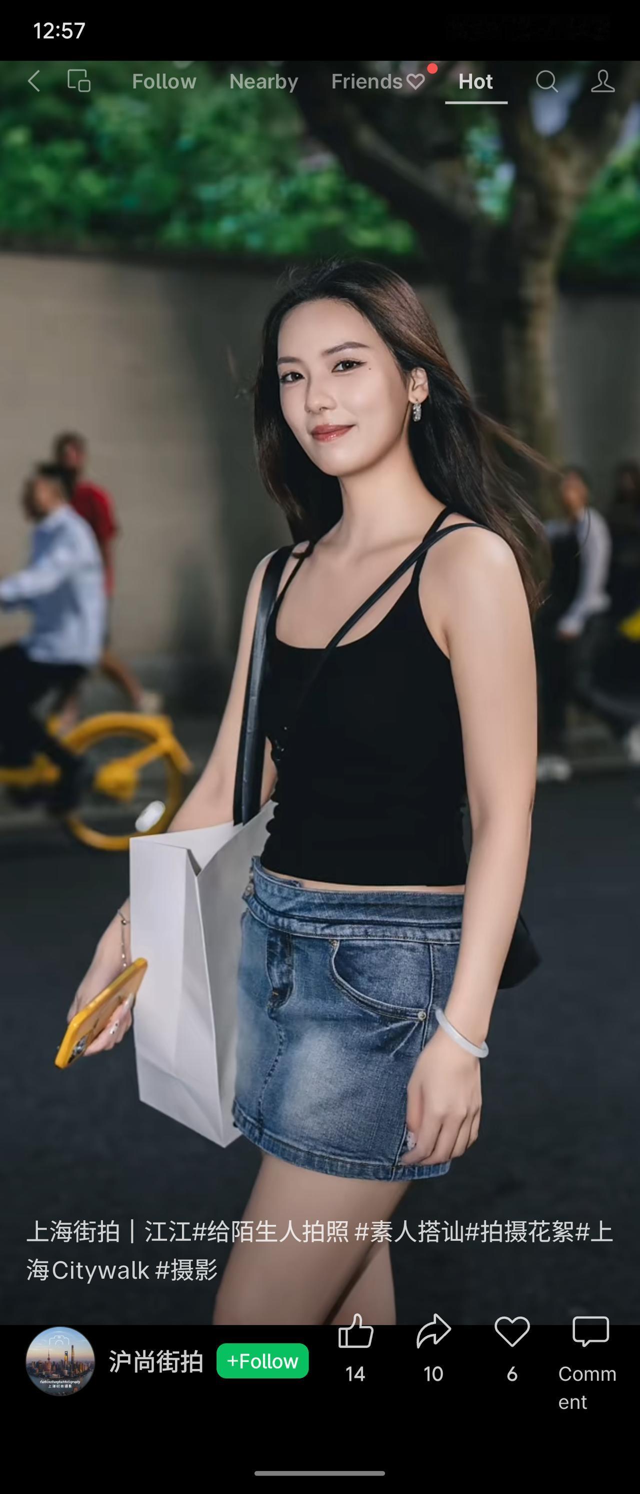 上海老街巷街拍，女生穿修身黑吊带搭配牛仔短裙，长发柔顺披肩，手提购物纸袋。笑容大