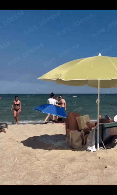 在乌克兰敖德萨海滩，一些游客在休闲游玩。而在离他们较远的海面上，一艘被俄军无人机