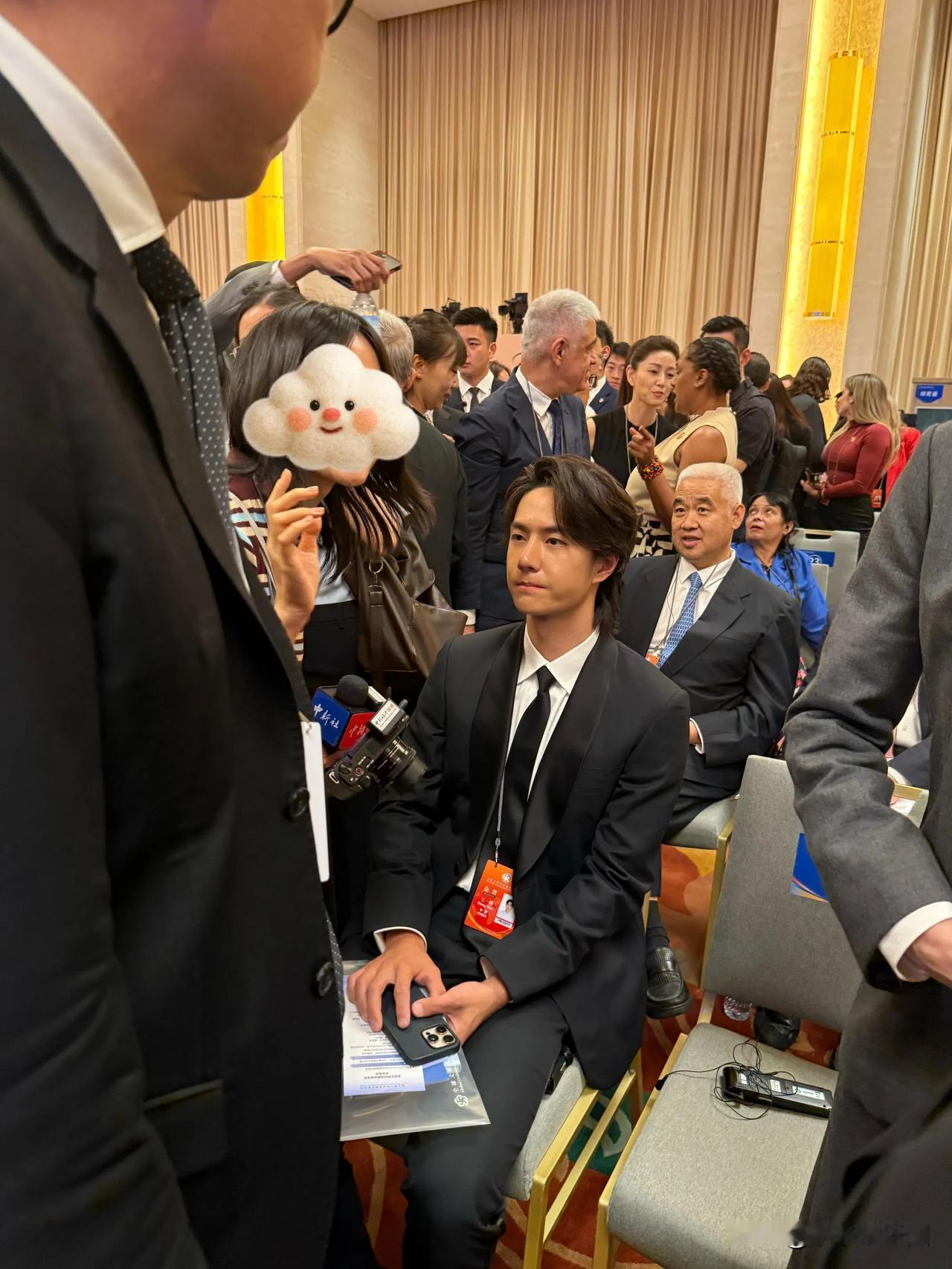 王一博素颜现身某重要活动现场。他身着一身笔挺西装，安静坐着，眼神专注看向镜头，那