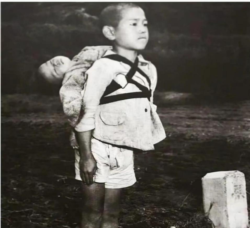 1945年，一名10岁的日本男孩抿着嘴，笔直地背着弟弟。而弟弟头向后仰，早已气绝