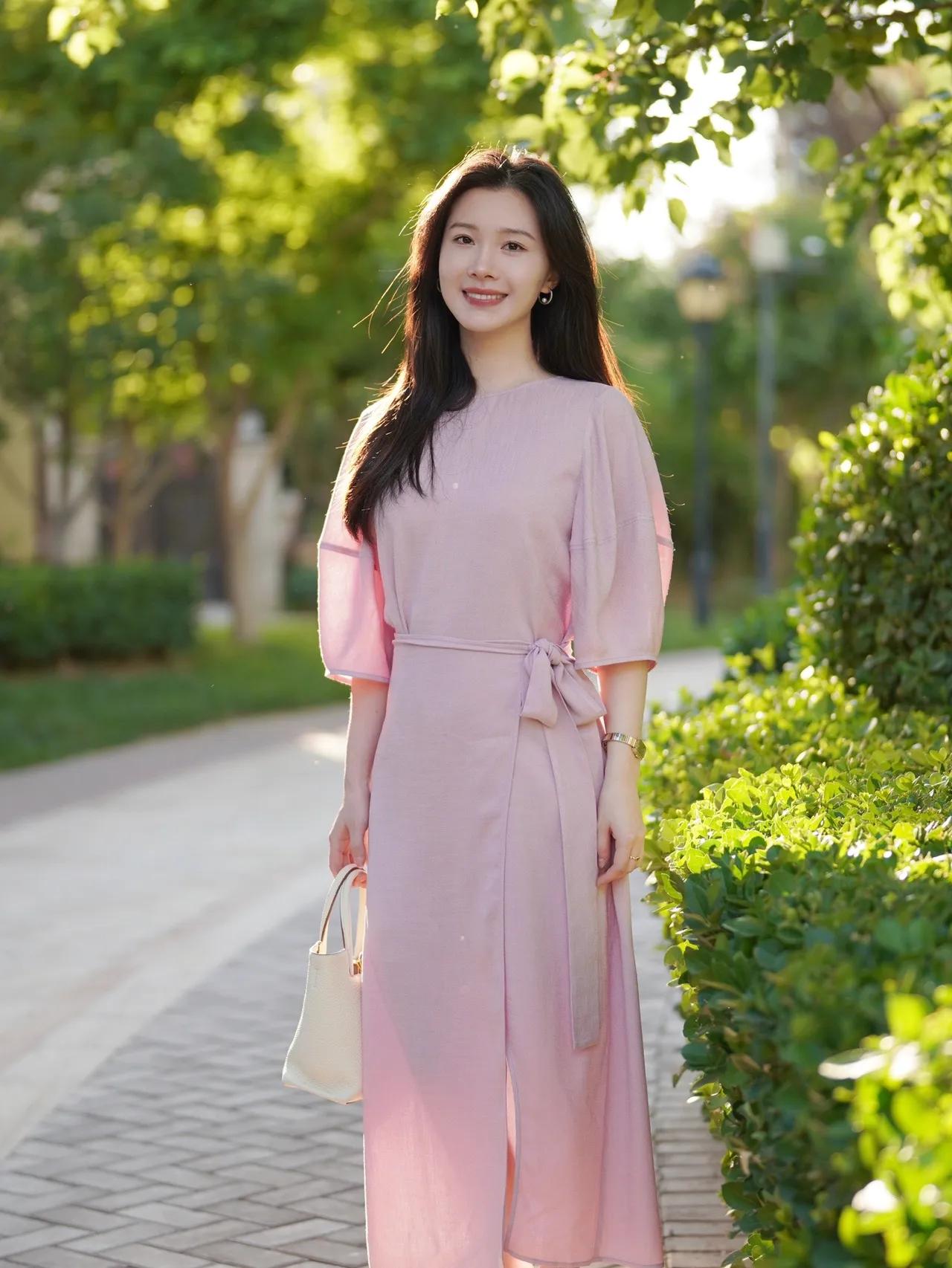 阳光明媚的午后，粉裙飘飘的少女漫步在绿意盎然的公园小径上。