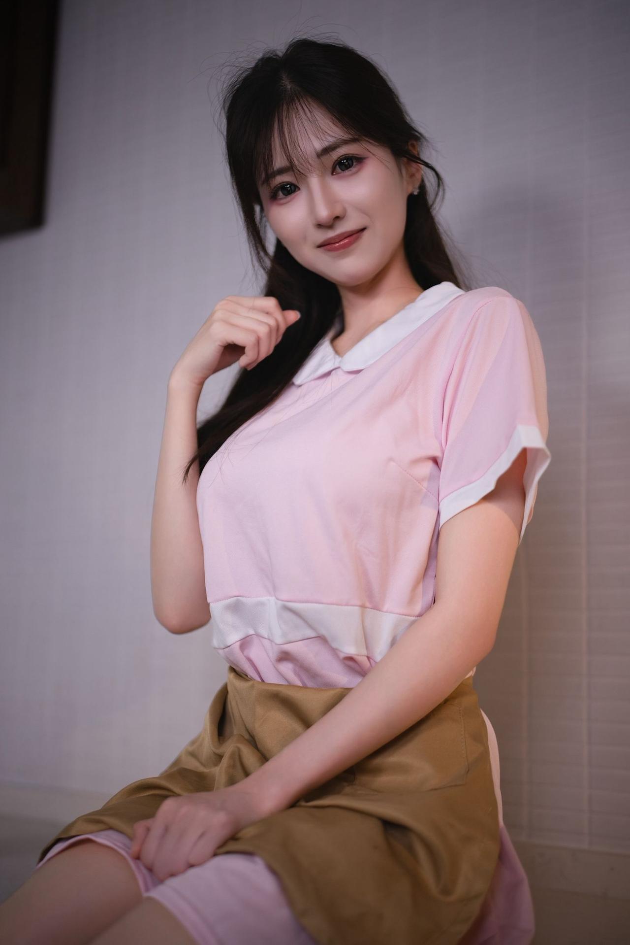 温柔甜美的少女，粉色上衣搭配棕色裙子，微笑着看向镜头。