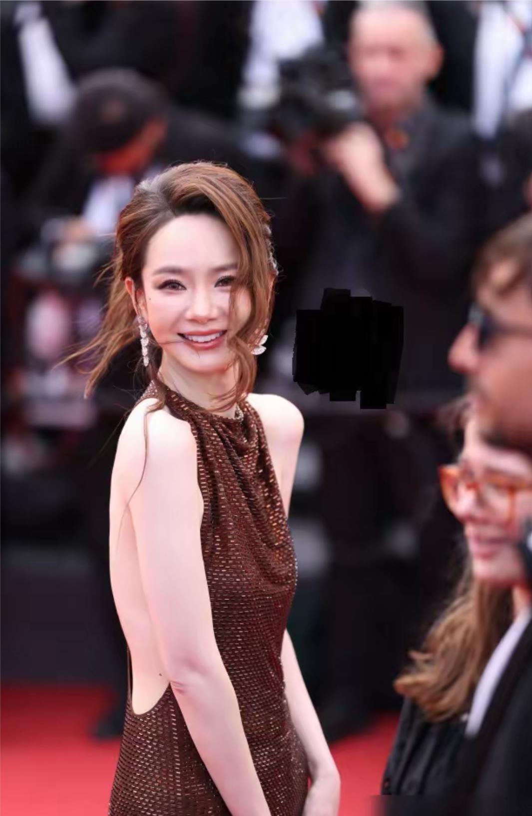 戚薇惊艳亮相戛纳红毯，穿着一件露背的棕色长裙，完美展现出她的高挑身材，扎着篷松的