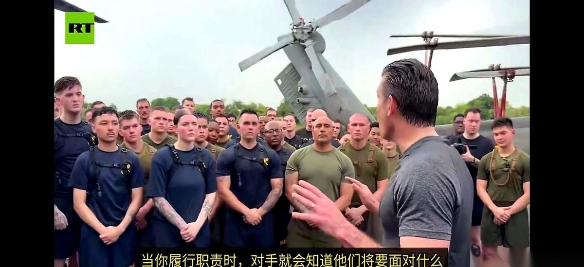 美国战争部长赫格塞斯，站在“拳师号”攻击舰的甲板上。他指着自己的胸口，对着台下