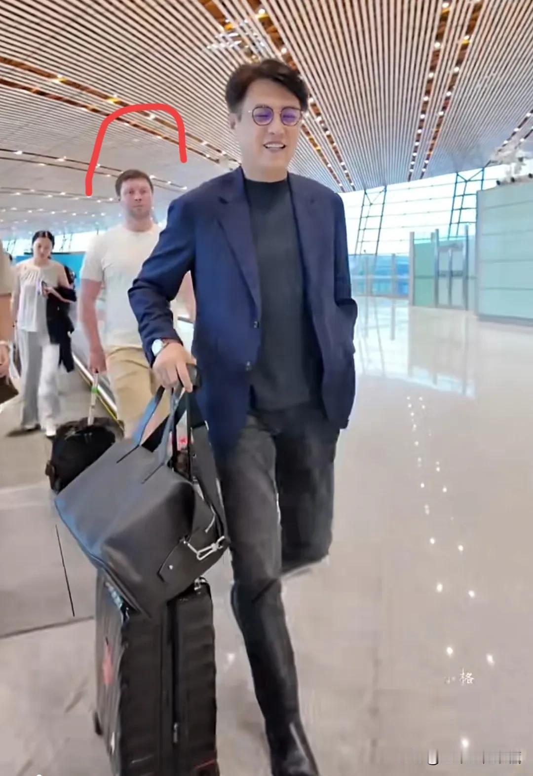 国民男神勒东现身机场，身穿蓝色西装外套，黑色牛仔裤，正装黑色皮鞋，戴着黑色框眼镜