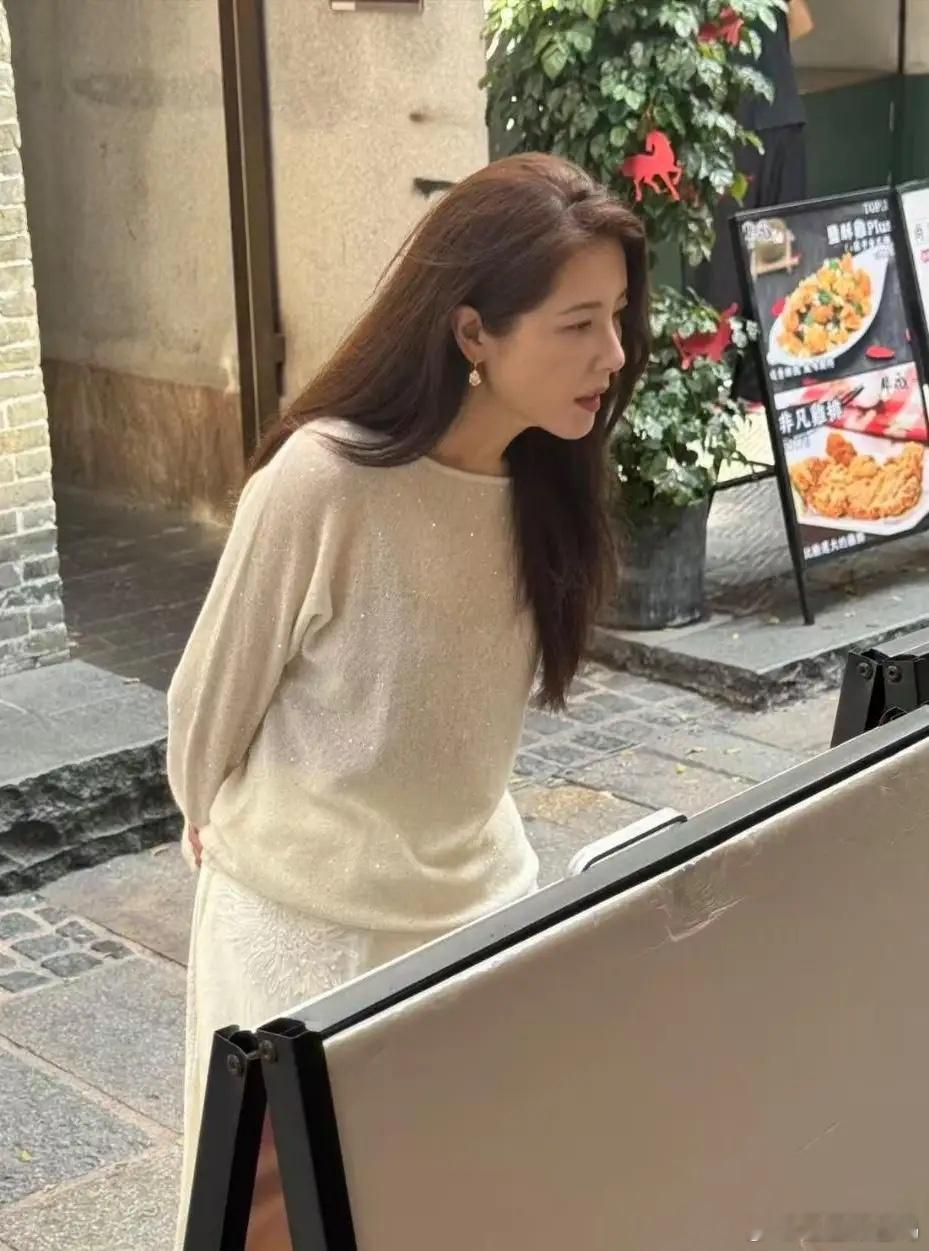 演员曾黎现身广东街头，她打扮朴素，她穿着白色裙子，一头棕色长发披肩，面色红润，身
