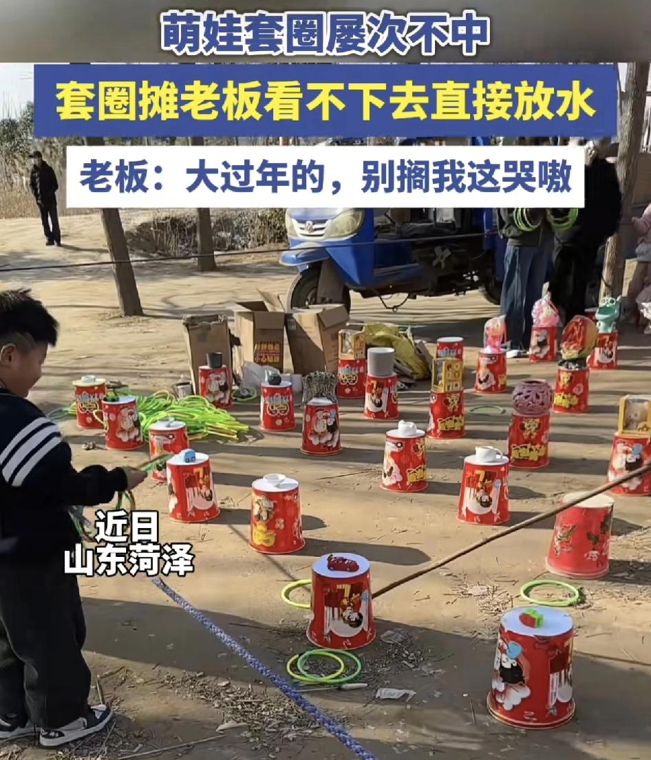 山东菏泽一套圈摊位，小男孩拿着手上一大捆的圈，一直都套不中自己喜欢的玩具，这时老