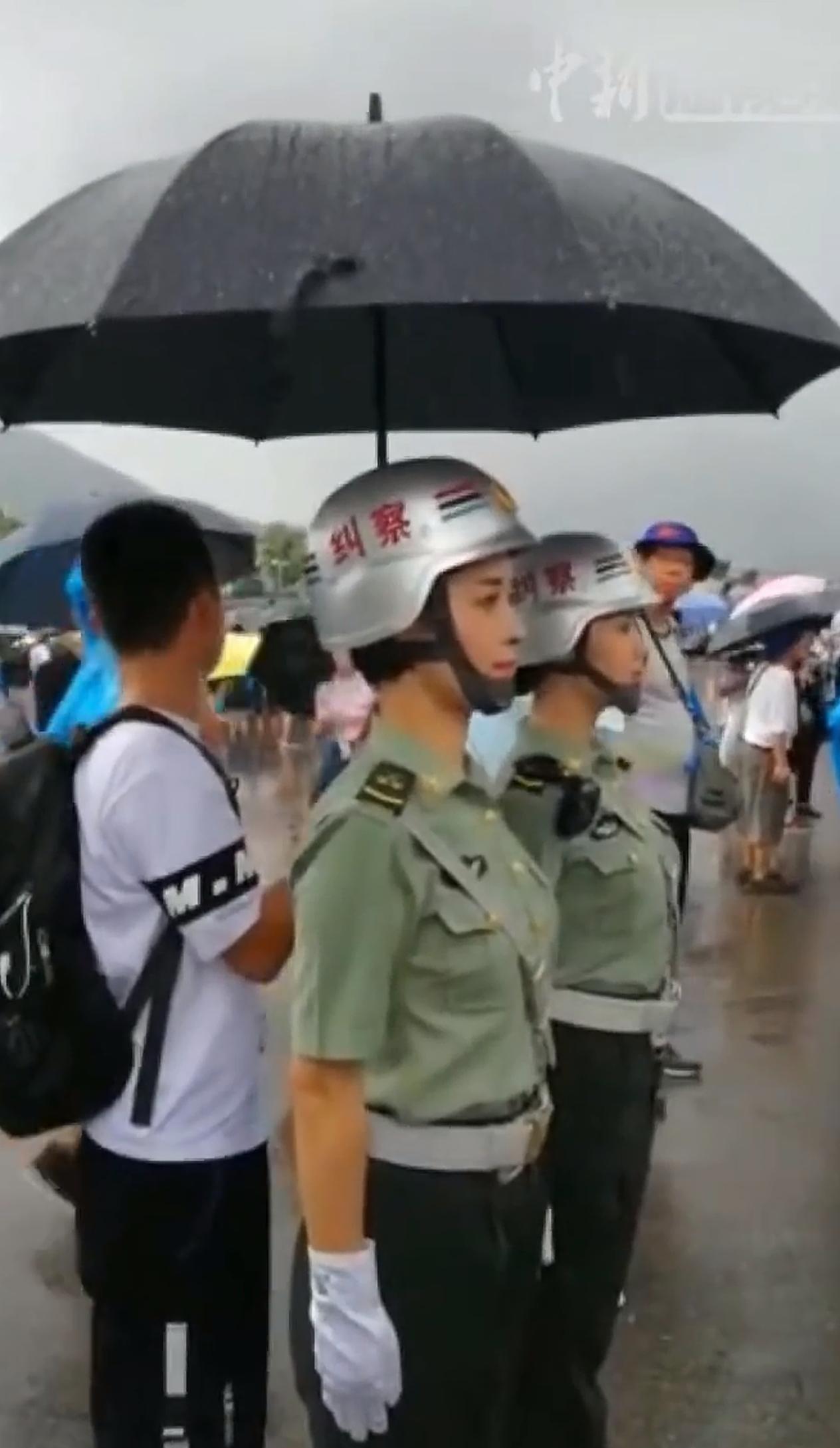 雨中，小伙为解放军驻香港部队执勤女兵撑伞，雨不停，人不走，真好！