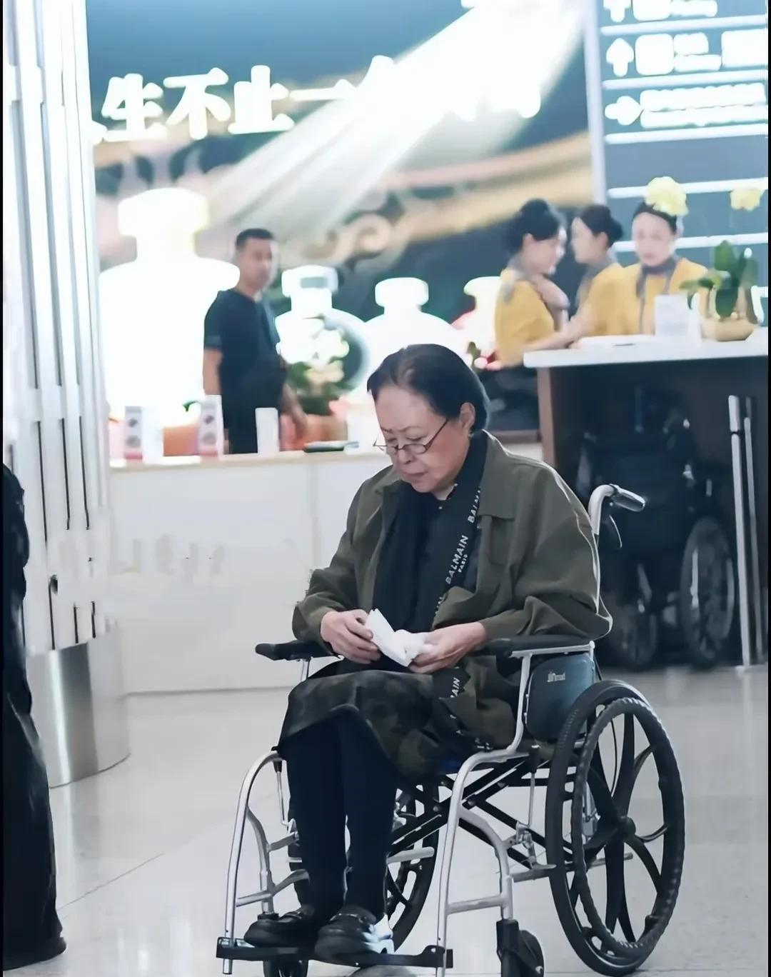 75岁的著名演员斯琴高娃，现身机场，坐着轮椅，头发稀疏，脸色暗沉，戴着老花镜，精