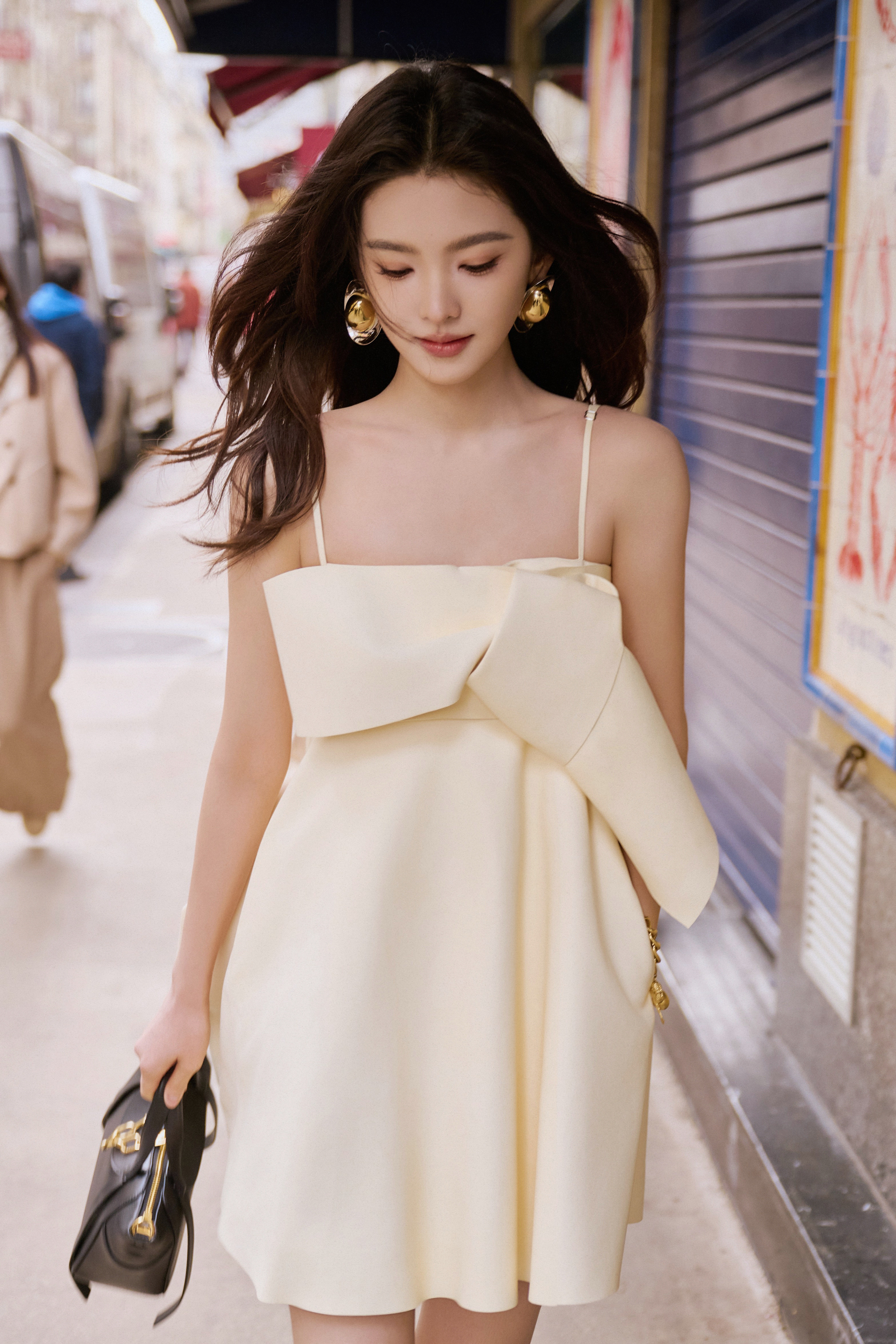 章若楠奶杏色抹胸裙揉碎了春日温柔，胸前立体蝴蝶结藏着恰到好处的娇俏，黑金撞色包