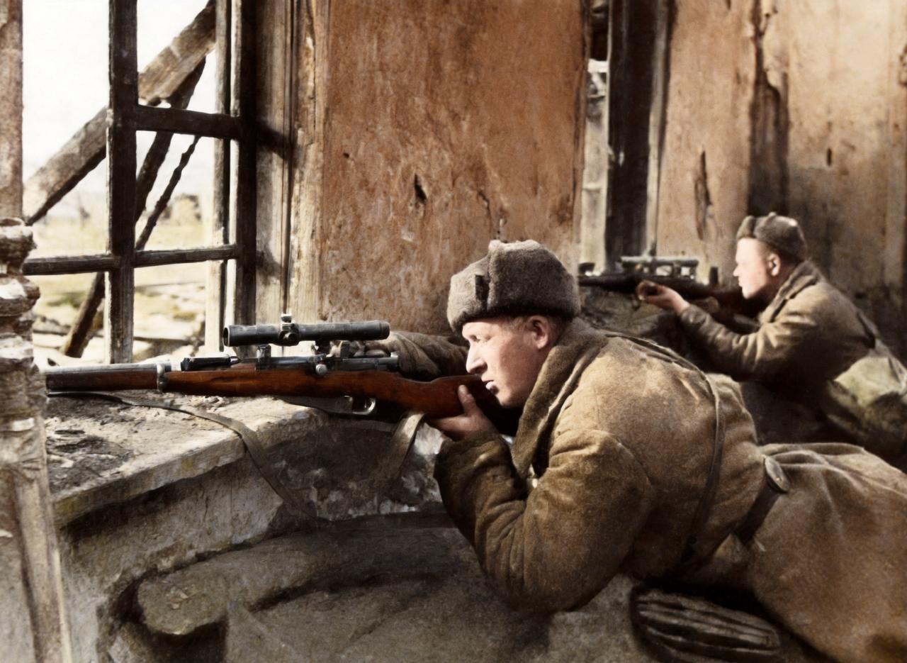 这是1942年斯大林格勒战役中两名苏军狙击手趴在一所破房子的窗户旁持枪向外瞄准。