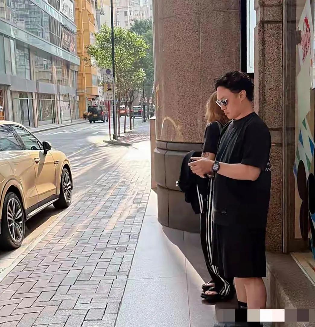 陈奕迅与妻子徐濠萦在香港街头等车：他一身黑色衣裤，戴着墨镜，身材偏胖，个矮腿短，