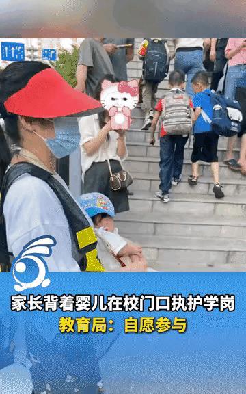 “太尴尬了！”广西百色，一女家长背着婴儿站在校门口执勤，戴着红帽子，捂着口罩，把