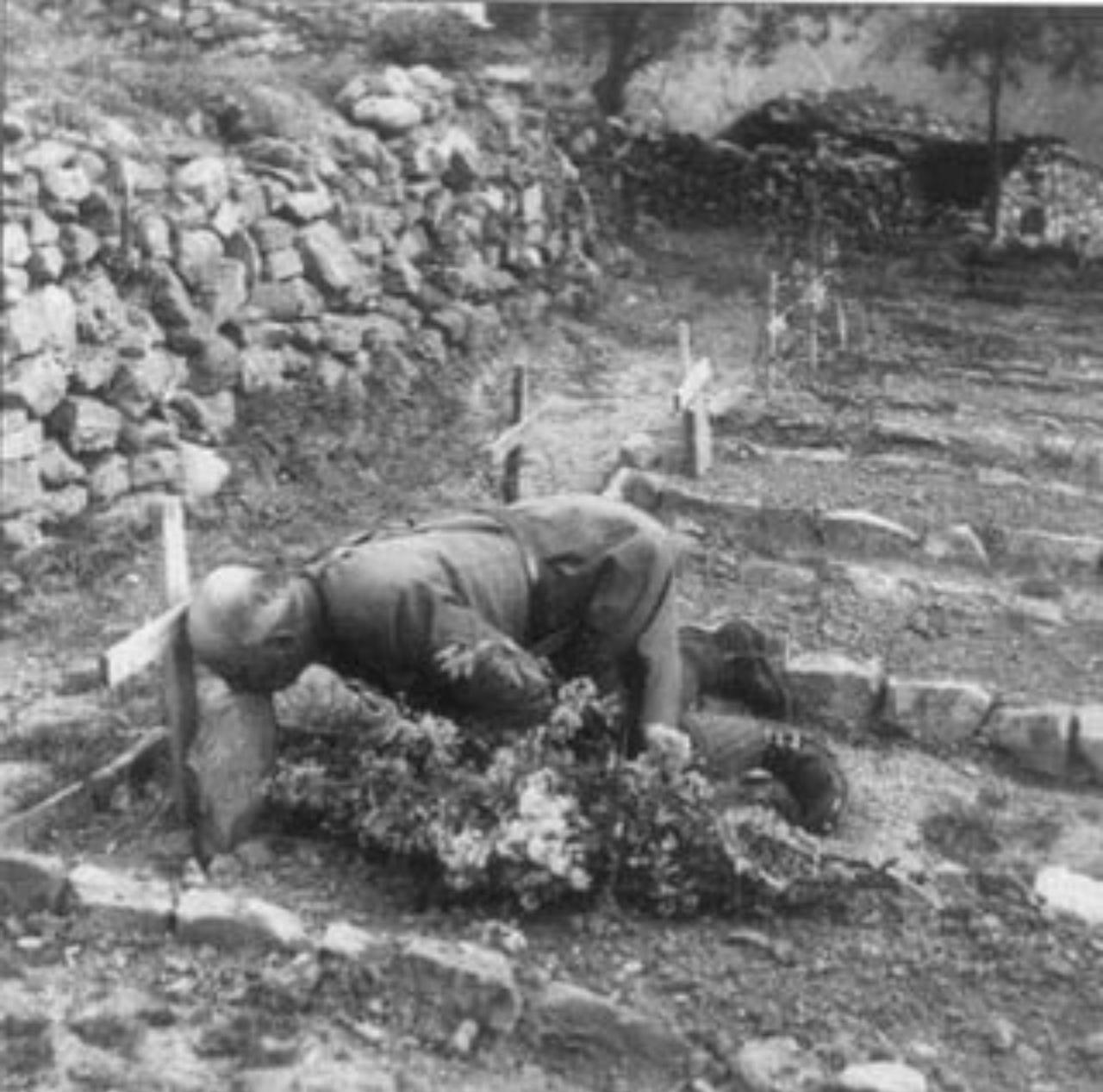 黑白照片显示，1941年，在阿尔巴尼亚前线一座石墙环绕的野战公墓里，一位秃顶的