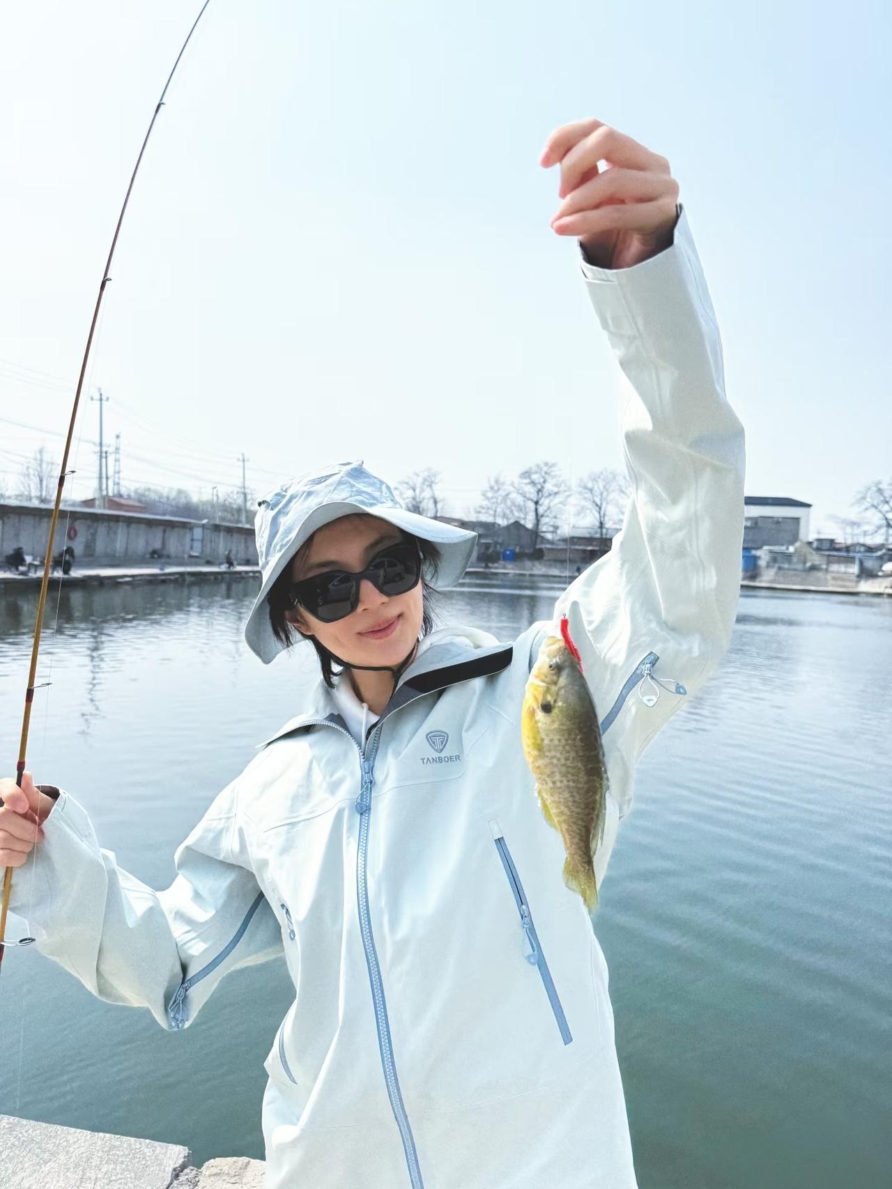 姚安娜穿着休闲，在湖边钓鱼，钓了一条小金鱼，还钓了一条略大一些的小银鱼。