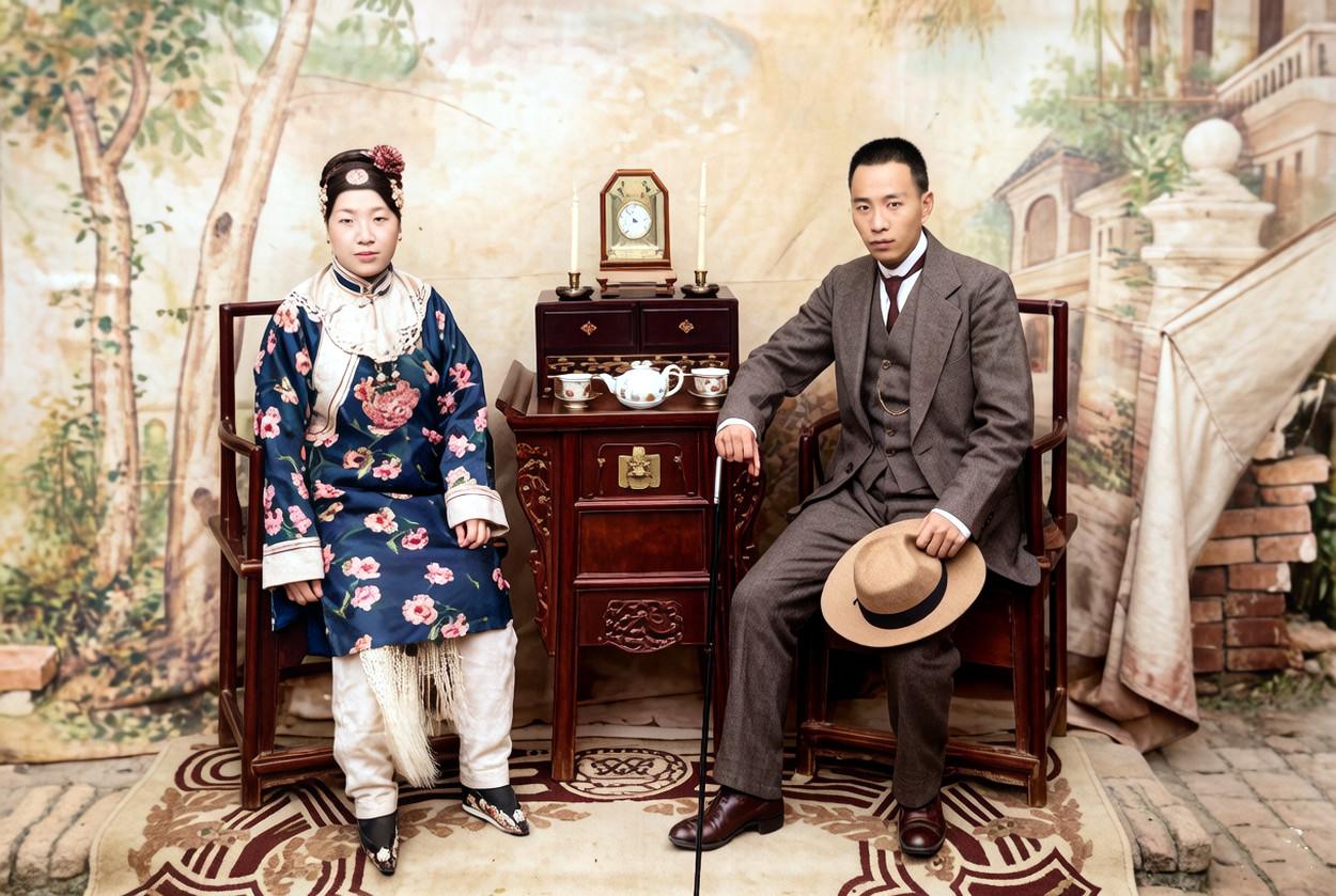 1920年，一对青年夫妇在照相馆内的合影。丈夫一身笔挺西装，手执文明棍与礼帽