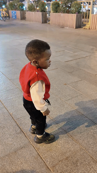 陕西西安街头，一个黑人小孩正在独自一个人路边玩耍。有一名骑摩托车的男子路过这里