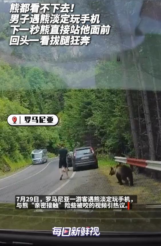 “这心也太大了！”一名男子站在路边专注看手机，一头棕熊从他身后悄悄靠近。熊先是凑