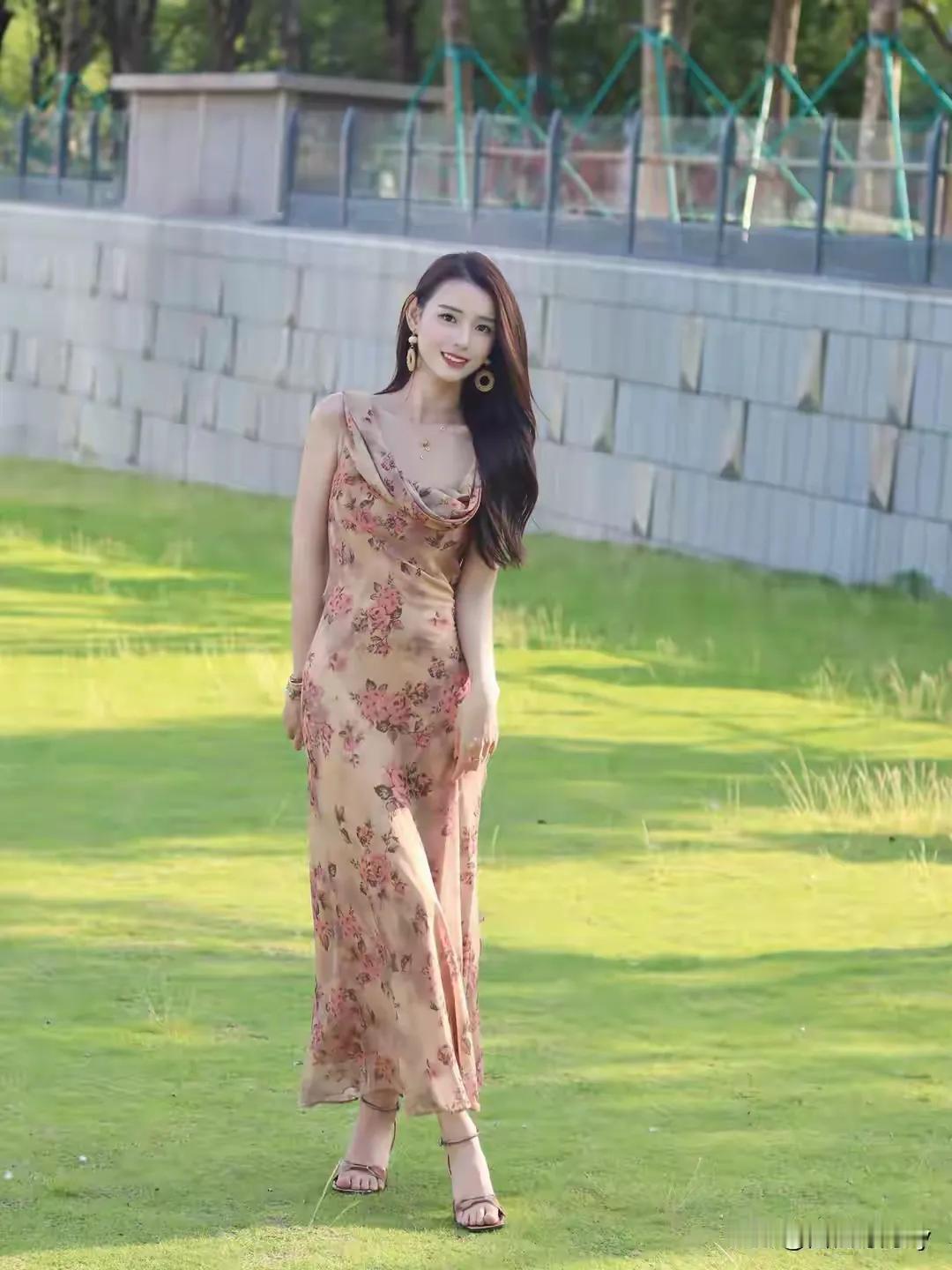 美女穿着花裙，站在草地上微笑。