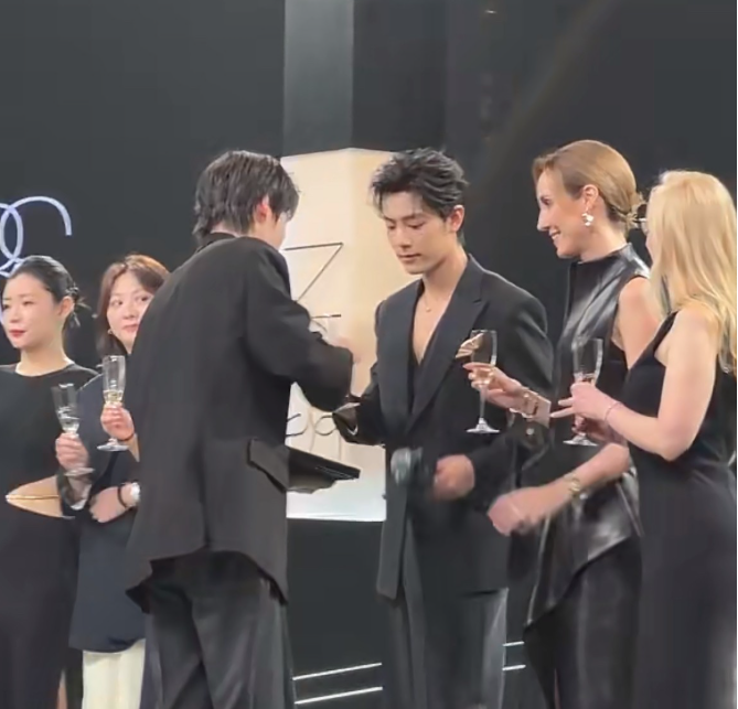 肖战左手边的两位女士离肖战比较近率先碰杯这过程中右边隔着硕大粉底液的女士也走了