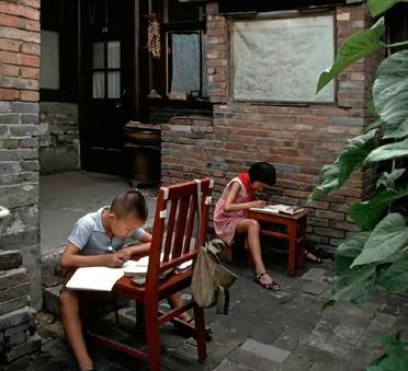 1981年，夏天的院子里，姐弟俩埋头写作业。弟弟坐在台阶上，将椅子当作桌子。姐姐